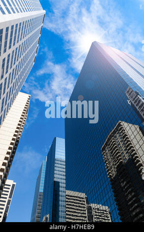 Tall skyscrapers contre un ciel bleu avec soleil peeking through créant un effet lens flare. Banque D'Images