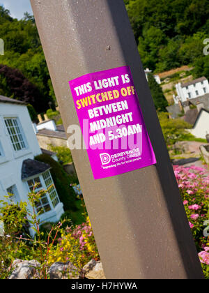 Cette lumière est éteinte entre minuit et 5h30 du signe sur un lampadaire dans une rue dans le Derbyshire, Angleterre, Royaume-Uni Banque D'Images