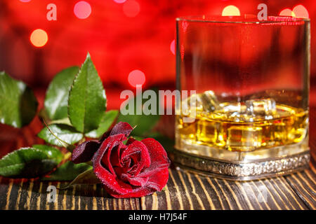 Verre de whisky écossais et de glace , rose rouge dans l'arrière-plan flou coloré de vacances sur table en bois Banque D'Images