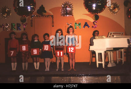 1969, historiques, l'époque de Noël et plusieurs jeunes filles line-up sur la scène à l'intérieur du camp de vacances Butlin à Littlehampton holiding numéros jusqu'avoir pris part à un concours de chant. Banque D'Images