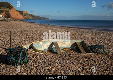 Un petit bateau presque ensevelis sous les bardeaux sur la plage de Sidmouth, Devon Banque D'Images