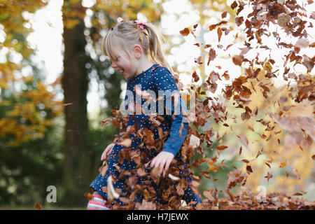 Professionnels de l'automne. Petite fille jouant dans les feuilles sèches pile en automne parc. Banque D'Images