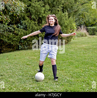 Jeune fille sur l'herbe botter un ballon de soccer et souriant Banque D'Images