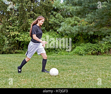Jeune fille sur l'herbe botter un ballon de soccer et souriant Banque D'Images
