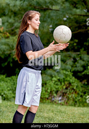 Jeune fille sur l'herbe de lancer un ballon de soccer et souriant Banque D'Images