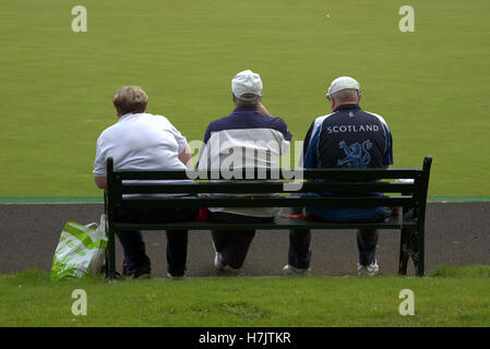 Trois hommes assis sur un banc avec grande pelouse veste logo Scotland background Banque D'Images