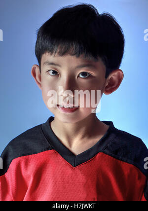 Asian boy portant un maillot sportif posant en studio, avec un éclairage spécial pour un côté. Isolé sur fond bleu Banque D'Images