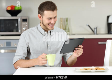 Homme heureux la lecture des nouvelles dans un comprimé pendant le petit-déjeuner dans la cuisine Banque D'Images