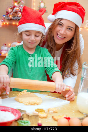 Portrait d'une mère aimante son petit fils d'enseignement pour faire des desserts, Porter du rouge Santa hats et making Christmas Cookies Banque D'Images