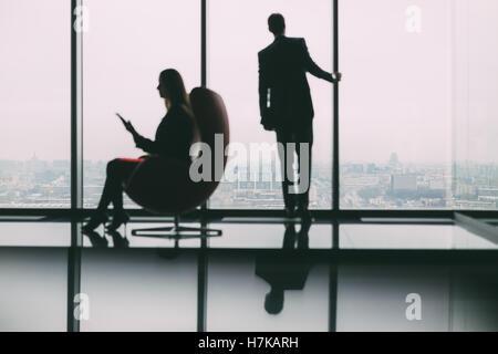 Silhouettes floues de businessman debout à côté de la fenêtre, regardant à l'extérieur de la ville, son collègue avec tablet Banque D'Images