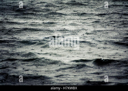 La pluie qui tombe sur la surface de l'eau. Close up de mer agitée avec des gouttes de pluie. Abstrait d'un détail. Banque D'Images