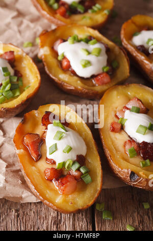 Pelures de pommes de terre farcies de fromage et bacon close-up sur la table rustique, vertical. Banque D'Images