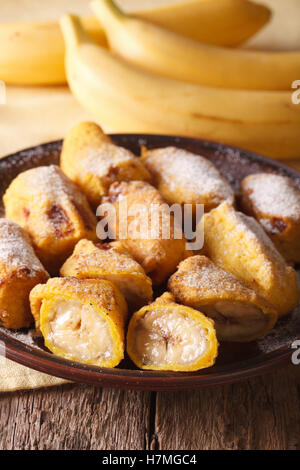 Bananes frites en pâte saupoudrée de sucre en poudre sur une assiette sur la table. La verticale Banque D'Images