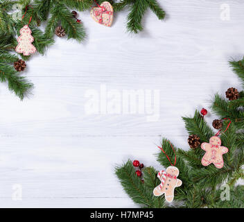 Fond en bois blanc avec des branches de sapin, des biscuits, des pommes de pin et baies rouges dans les coins pour Noël concept. Banque D'Images