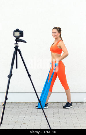 Jeune femme sportive videoblogger faisant des exercices de renforcement de base en utilisant des bandes de latex dans un concept de santé et de style de vie, smiling Banque D'Images