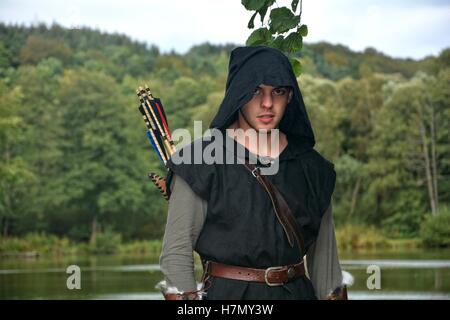 Archer médiéval avec capot noir et couleur des flèches dans le carquois se tient devant un lac et regarde vers l'avant Banque D'Images