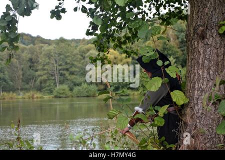 Archer médiéval avec capot noir est caché derrière arbre dans le lac avec courbe tendue Banque D'Images