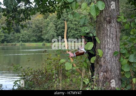 Archer médiéval avec capot noir est caché derrière arbre dans le lac avec courbe tendue Banque D'Images