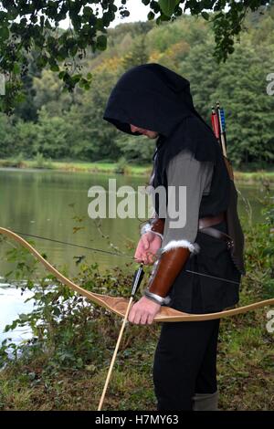 Archer médiéval avec capot noir se tient avec courbe tendue et avec des flèches dans le lac et regarde vers le bas Banque D'Images