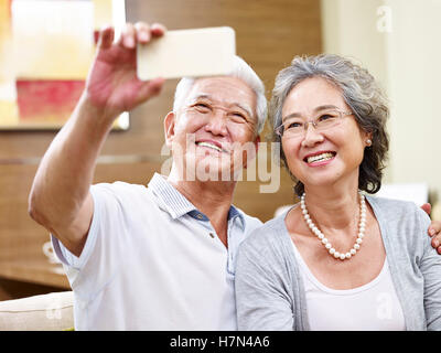 Senior asian couple en tenant un téléphone cellulaire à la maison en utilisant des selfies Banque D'Images