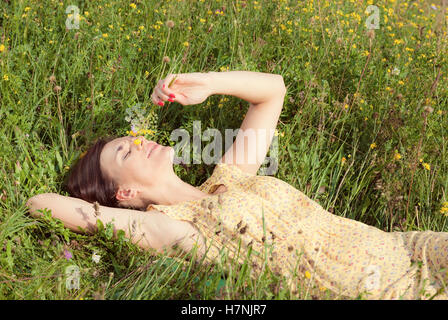 Belle fille couchée sur domaine de l'herbe verte et la tenue des fleurs dans sa main Banque D'Images