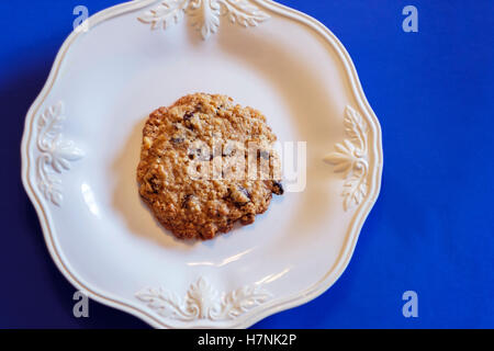 Un seul témoin à l'avoine et aux raisins faits maison avec les noix sur une plaque blanche, fond bleu. Tourné à partir de ci-dessus. USA Banque D'Images