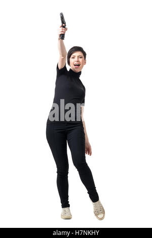 Jeune femme espion dans des vêtements noirs avec tir jusqu'à l'air. La pleine longueur du corps portrait studio isolated over white background. Banque D'Images