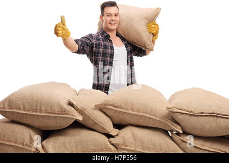 Les jeunes travailleurs agricoles derrière une pile de sacs de jute tenant un sac sur son épaule et un thumb up isolated on white b Banque D'Images