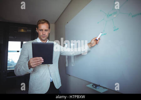 Businessman looking at digital tablet lors de l'écriture sur tableau blanc Banque D'Images