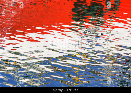 Bouclier (crash) pneu en caoutchouc sur coque de bateau, réflexions colorées (bleu blanc rouge) sur la surface de l'eau. Banque D'Images