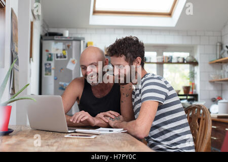 Gay couple using laptop in kitchen Banque D'Images