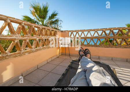 Pieds de l'homme de vous détendre sur une chaise longue, mer balcon, station touristique populaire de l'île de Zakynthos, Grèce Banque D'Images
