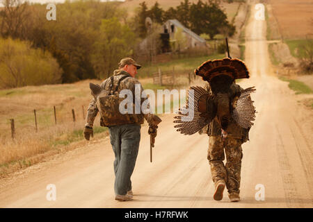 Les chasseurs Turquie transportant les dindes mortes Walking on Country Road Banque D'Images