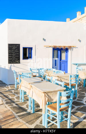 Des tables avec des chaises dans taverne grecque à Naoussa port, l'île de Paros, Grèce. Tableau de menu sur le mur indique les noms de plat avec des prix. Banque D'Images