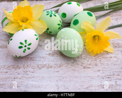 Vert et blanc, les oeufs de pâques décorés par des points et des fleurs et des jonquilles sur la planche de bois blanc Banque D'Images