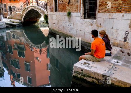 Un couple assis par un canal Venise Italie Banque D'Images