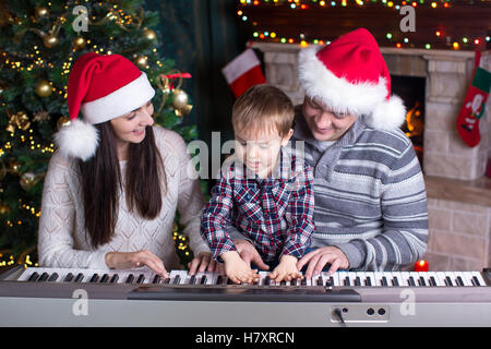 Famille - mère, père et enfant wearing santa hats jouant du piano sur fond de noël festival Banque D'Images