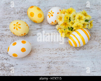 Le blanc et le jaune des oeufs de pâques décorés par des rayures, des points et des fleurs et bouquet primrose sur le fond blanc Banque D'Images