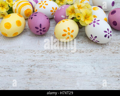 Blanc, violet et jaune d'oeufs de pâques décorés par des rayures, des points et des fleurs et la primevère sur la planche de bois blanc Banque D'Images