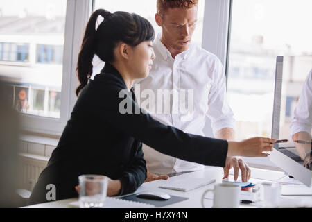 Young Asian businesswoman pointing at l'écran du bureau et montrant quelque chose à collègue masculin. Les gens d'affaires travailler ensemble je Banque D'Images