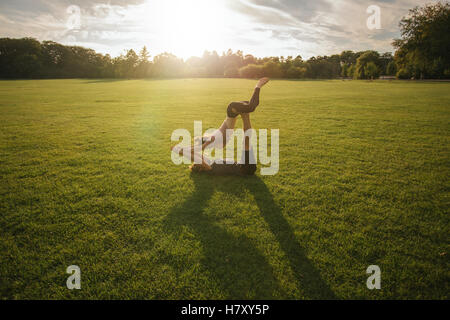 Piscine shot of young man and woman doing yoga en paire. Couple d'entraînement yoga acrobatique sur pelouse. Banque D'Images