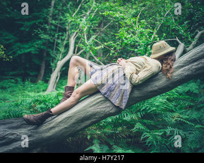 Une jeune femme est couché sur un arbre tombé dans la forêt entouré de fougères avec un safari hat couvrant son visage Banque D'Images