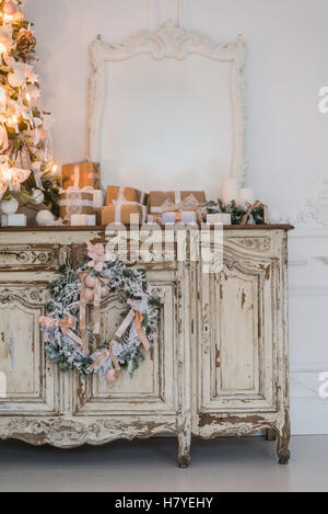 Arbre de Noël sur une commode en bois commode bureau en intérieur blanc, décorée avec des fleurs artificielles, des guirlandes et des jouets Banque D'Images