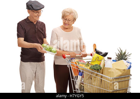 Homme mature montrant un paquet de pommes pour une femme âgée avec un panier plein de provisions isolé sur fond blanc Banque D'Images