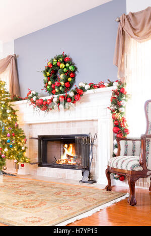 Cheminée de Noël avec guirlande, guirlande colorée , un arbre décoré et un fauteuil confortable en face d'un feu ardent Banque D'Images