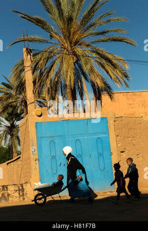 Maroc, Tinejdad, Vallée du Todra, Ksar El Khorbat, femme poussant la brouette avec des enfants qui suivent, un Ksar est un village entouré de murs, Banque D'Images