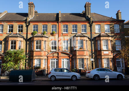 Vue avant d'une propriété victorienne anglaise classique à trois étages d'appartements avec des voitures garées en face de c Banque D'Images