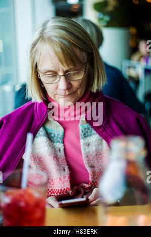 Femme assise au restaurant de l'intérieur contrôle son café smart phone ; l'Aéroport International de Denver, Denver, Colorado, USA Banque D'Images
