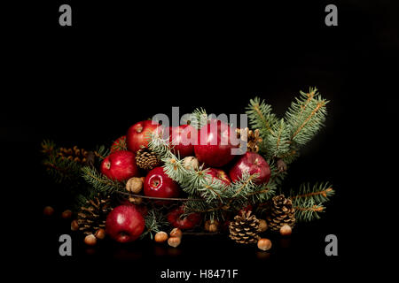 Noël et Nouvel an. Des pommes avec des pommes de pin et les écrous dans un panier avec des branches de sapin. Cadeaux et bougies. Banque D'Images