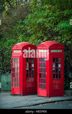 Paire de cabines téléphoniques rouge classique se tenir sous la verdure au bord d'un parc à Londres, Angleterre, RU Banque D'Images